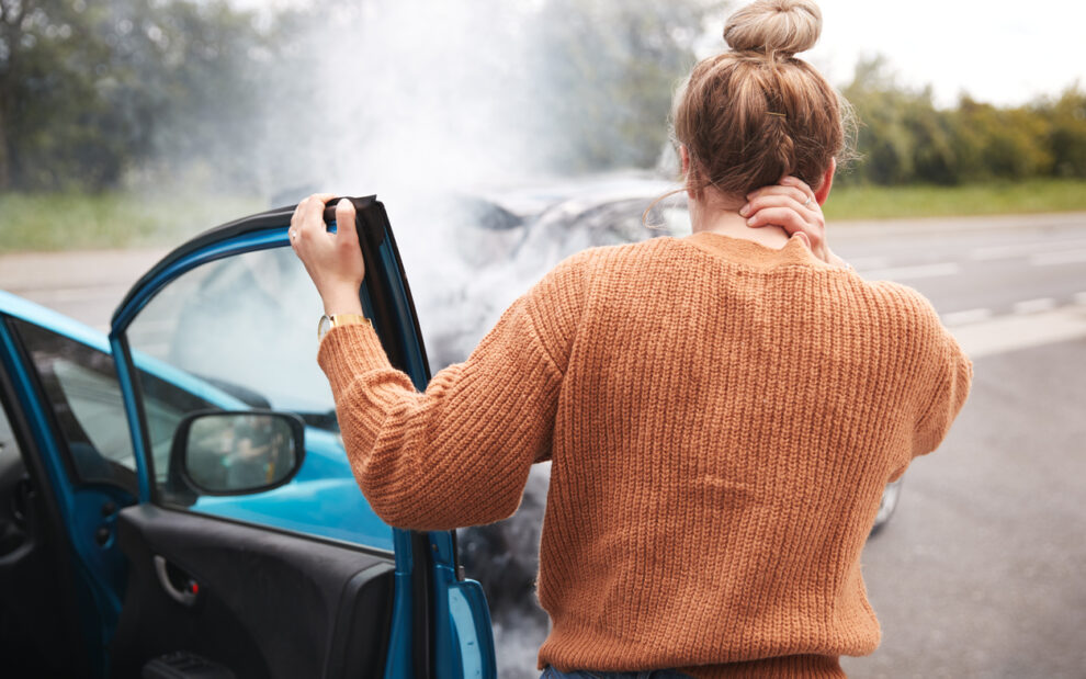 Rear View Of Female Motorist With Head Injury Getting Out Of Car After Crash