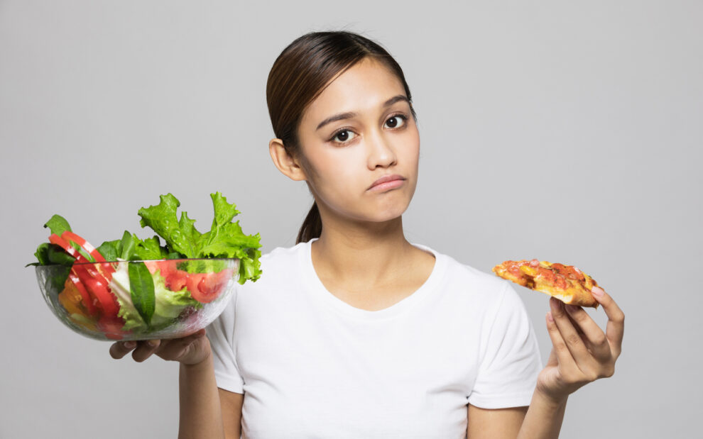 Young Woman Holding Up a Bowl of Salad and Slice of Pizza